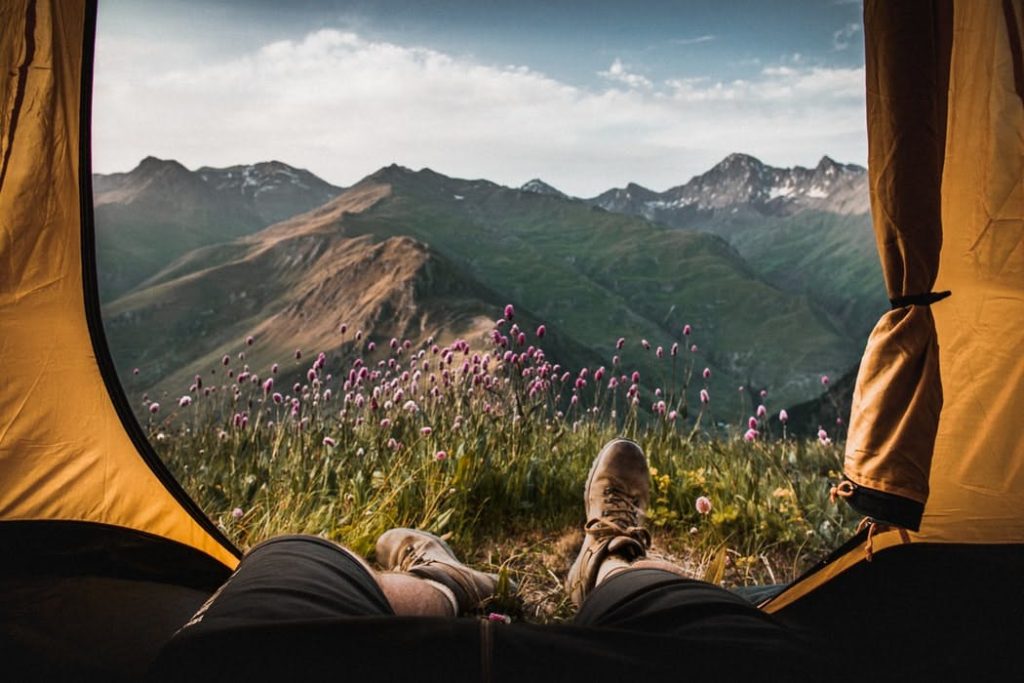 Camping: Beine und Füße einer Person, die in einem geöffneten Zelt liegt, Blick über bergige Landschaft 