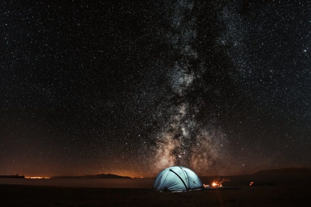 Camping: Blaues, beleuchtetes Zelt in der Dunkelheit unter dem sternenklaren Himmel mit der Milchstraße