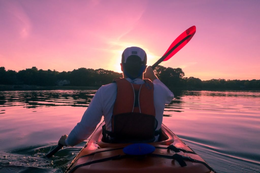 Mann im Kanu paddelt auf einem See in der Mecklenburgischen Seenplatte im Sonnenuntergang und der Sonne entgegen 