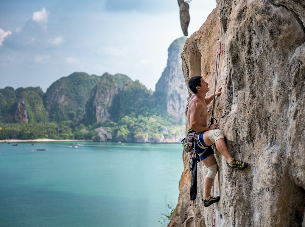 Rock climber with Thai coastline in background