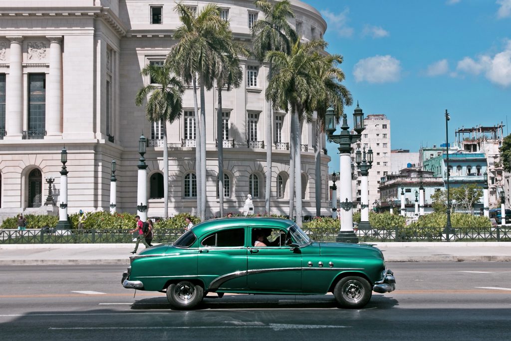 A green old timer driving through Cuba. 