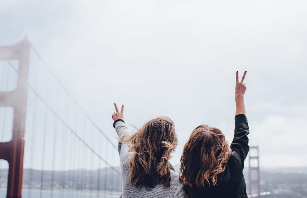 2 Frauen, die vor der Golden Gate bridge in San Fransisco stehen mit dem Rücken zur Kamera, glücklich, weil sie die perfekte Reisepartnerin gefunden haben.