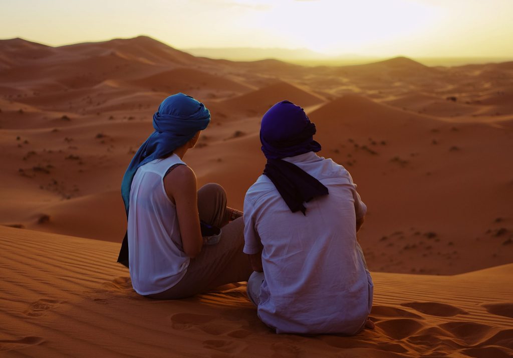 2 Reisepartner, die zusammen in der Wüste sitzen und glücklich sind, dass sie sich gefunden haben.