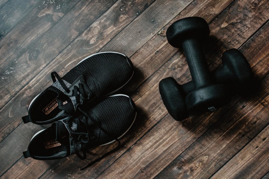 Ein Paar schwarze Sportschuhe mit zwei schwarzen Hanteln auf dunklem Holzboden 