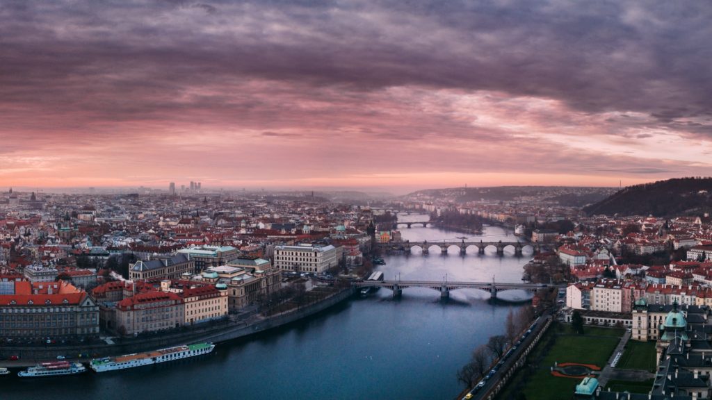 Prag fotografiert aus der Vogelperspekktive im Sonnenaufgang. Zu sehen ist die Karlsbrücke und viele weitere architektonisch beeindruckende Gebäude aus dem Mittelalter