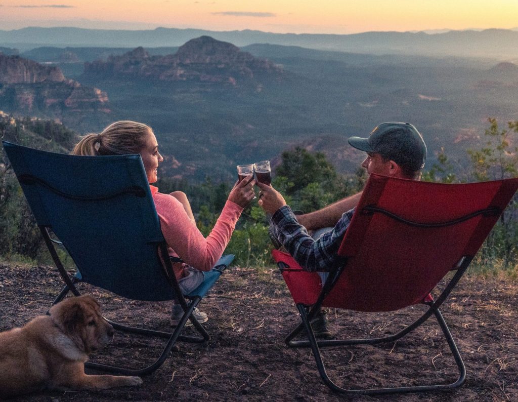 A man and woman toasting with wine and listening to Amazon Music during their camping trip.