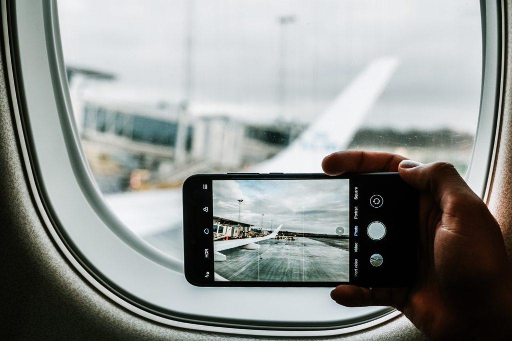 best travel apps - a phone being held taking a picture outside the window of a plane 
