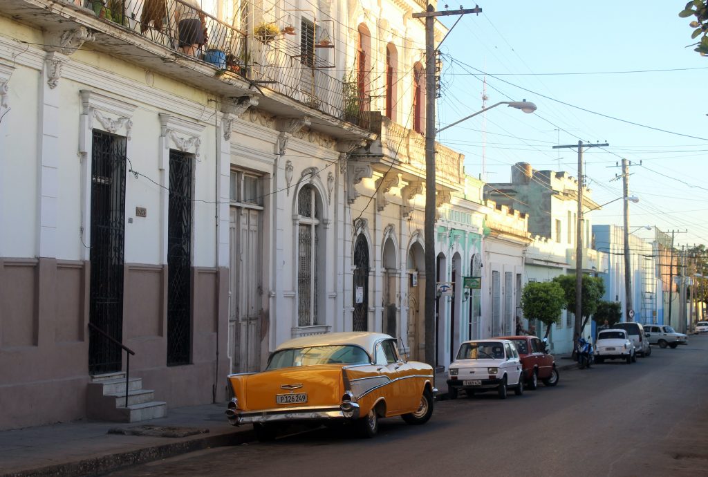 Cienfuegos with white buildings and a yellow vintage car parked in front.