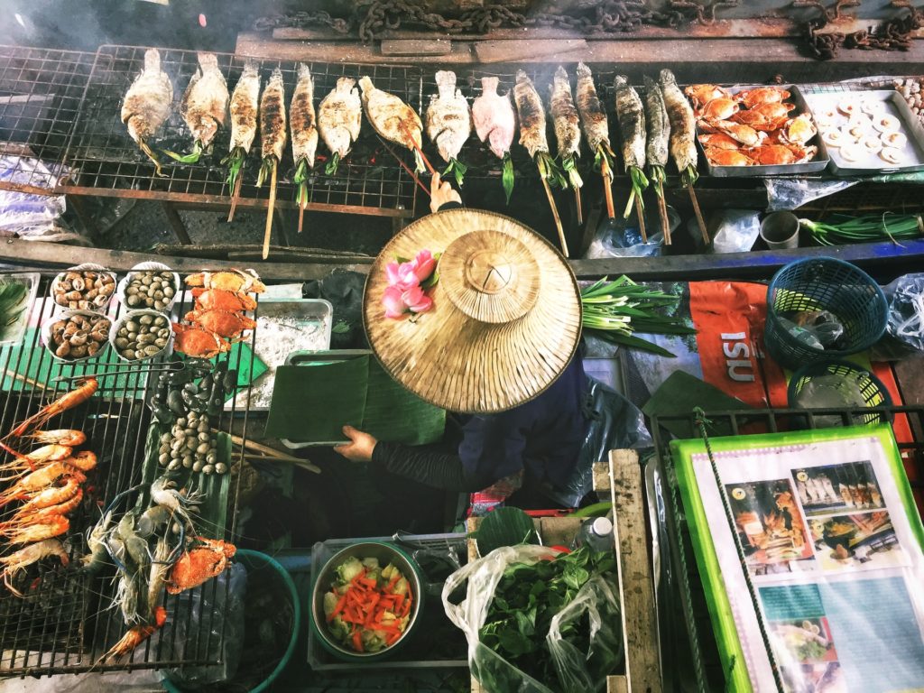 picture of person wearing a rice hat whilst cooking street food in asia, different street foods found when backpacking asia 