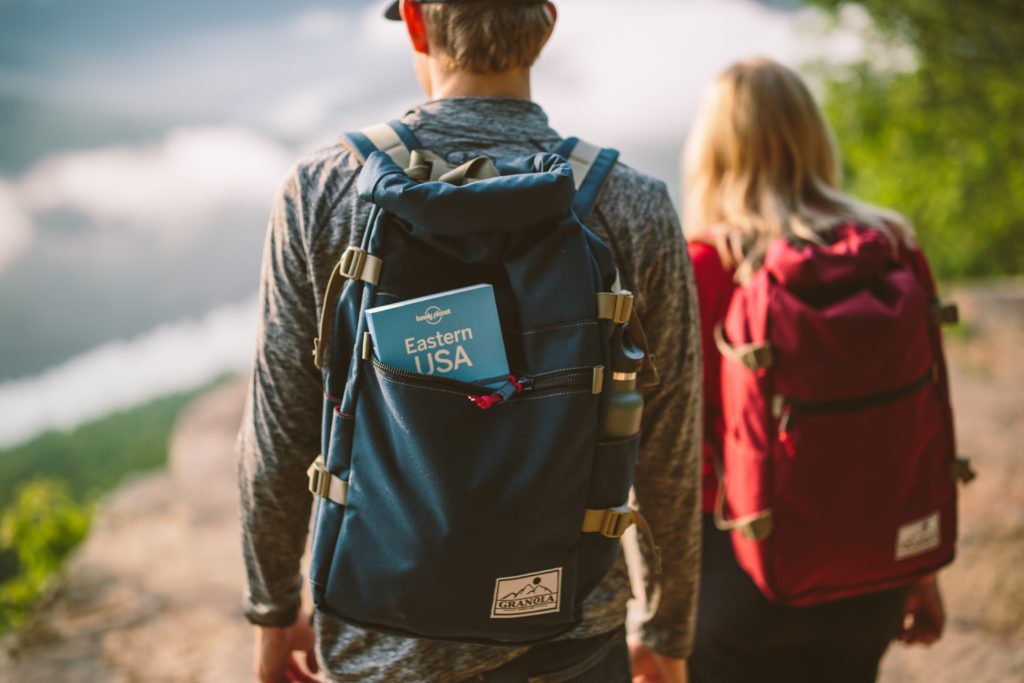 two travelers wearing backpacks with blue travel book