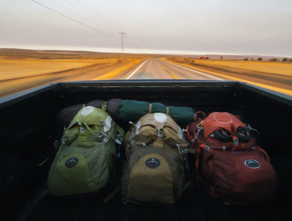3 guys sitting behind a car outside with 3 backpacks on fun ways to go abroad adventure.