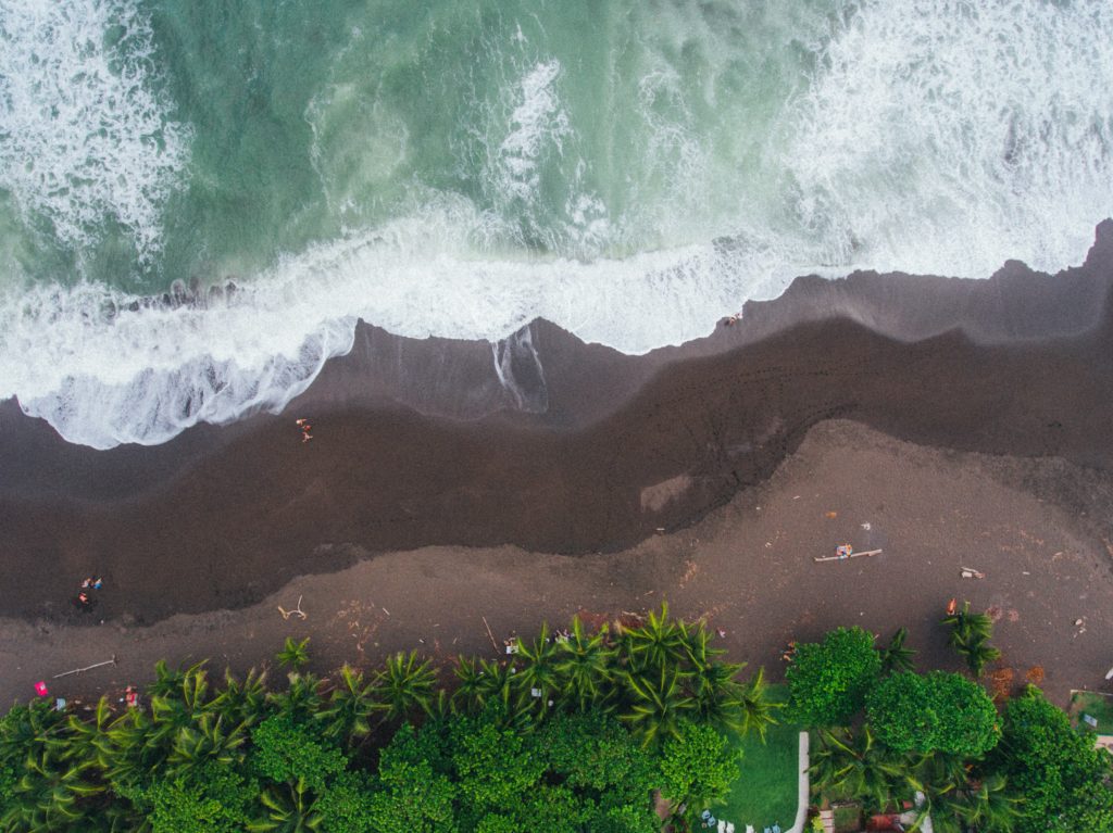 ein Strand in Costa Rica mit dunklem Sand und hellem Wasser mit grünen Bäumen im Hintergrund. 