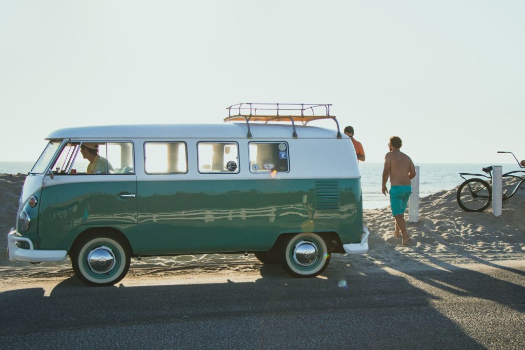 Green and white camper van at the beach with people around tips for road trip