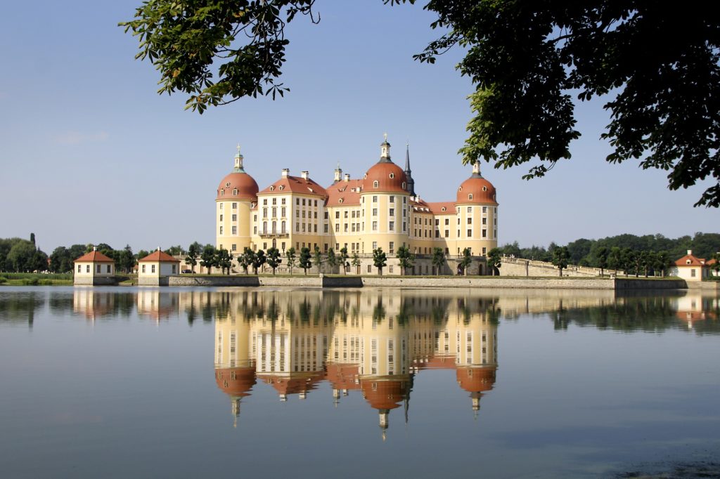 Moritzburg Castle in Saxony which is white and has red roof surrounded by water