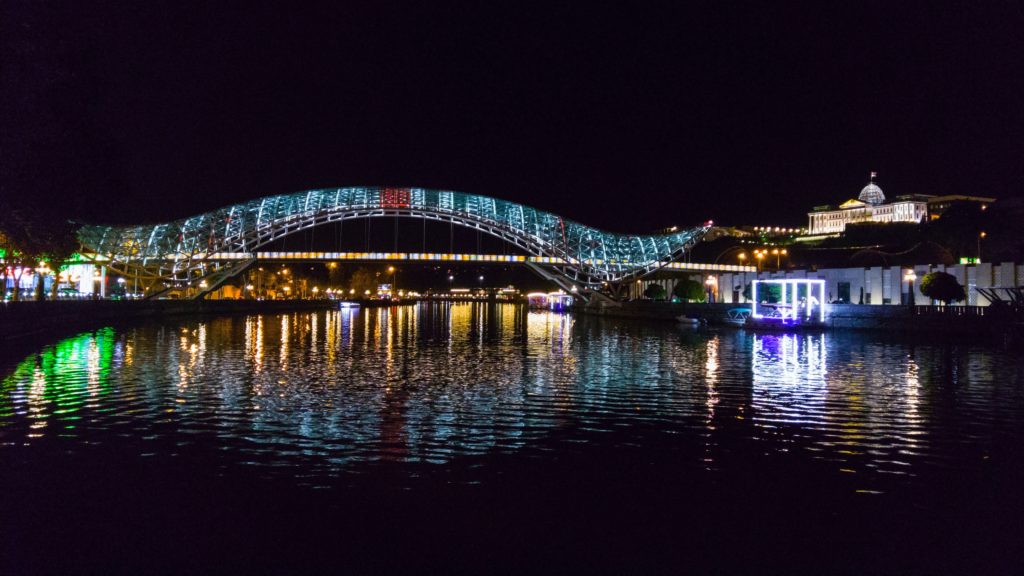 Die Hauptstadt Georgiens in der Nacht mit einer Brücke die beleuchtet ist 
