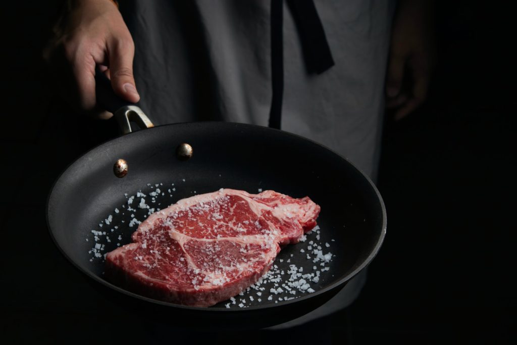 a person holding a frying pan with steak in it, covered in salt which is a famous argentinian dish