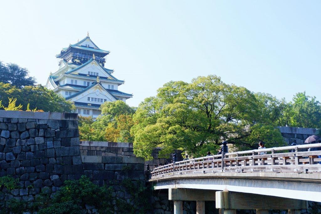 Osaka-jo castle and museum in Japan during the day with green trees around and a bridge.