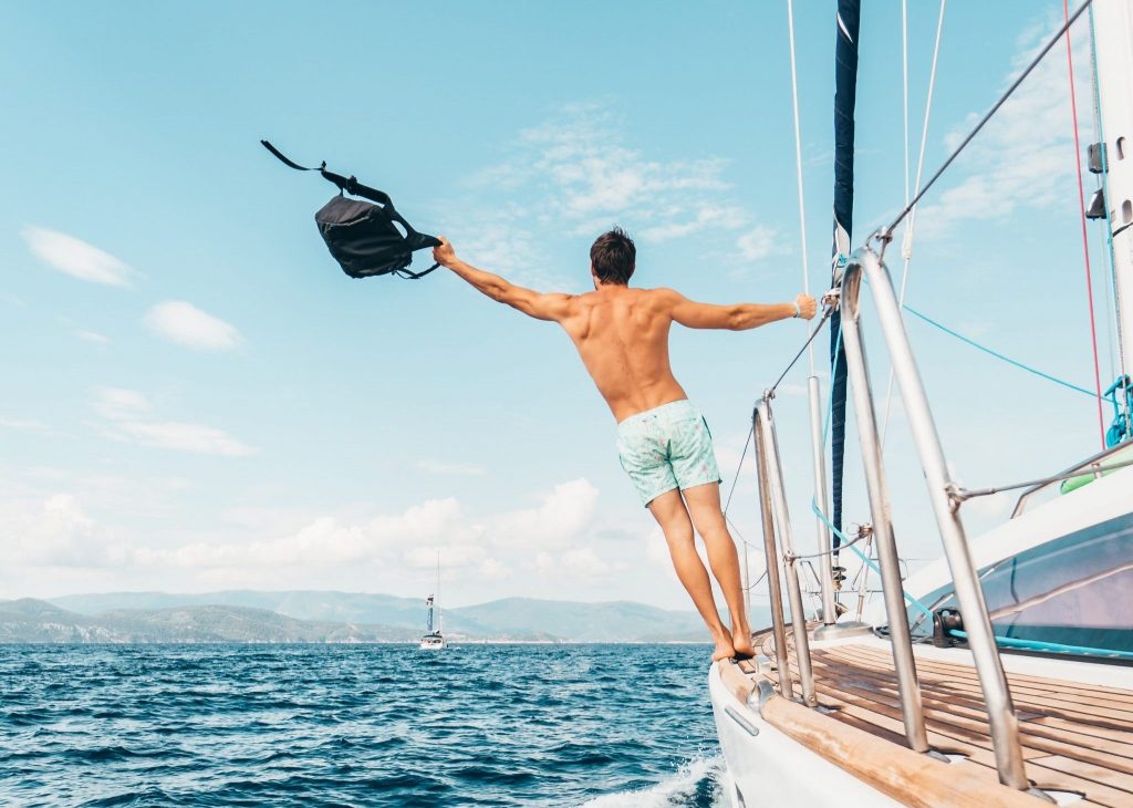 A man leans far over the railing of a boat, holding the waterproof backpack.