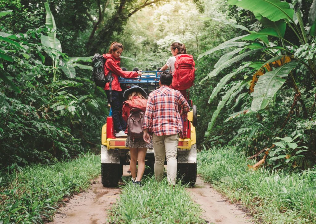 Gruppe von Reisenpartnern im Dschungel an einem Geländefahrzeug