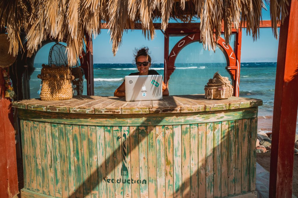 Eine Frau sitzt mit ihrem Laptop an einer Strandbar aus Schilf
