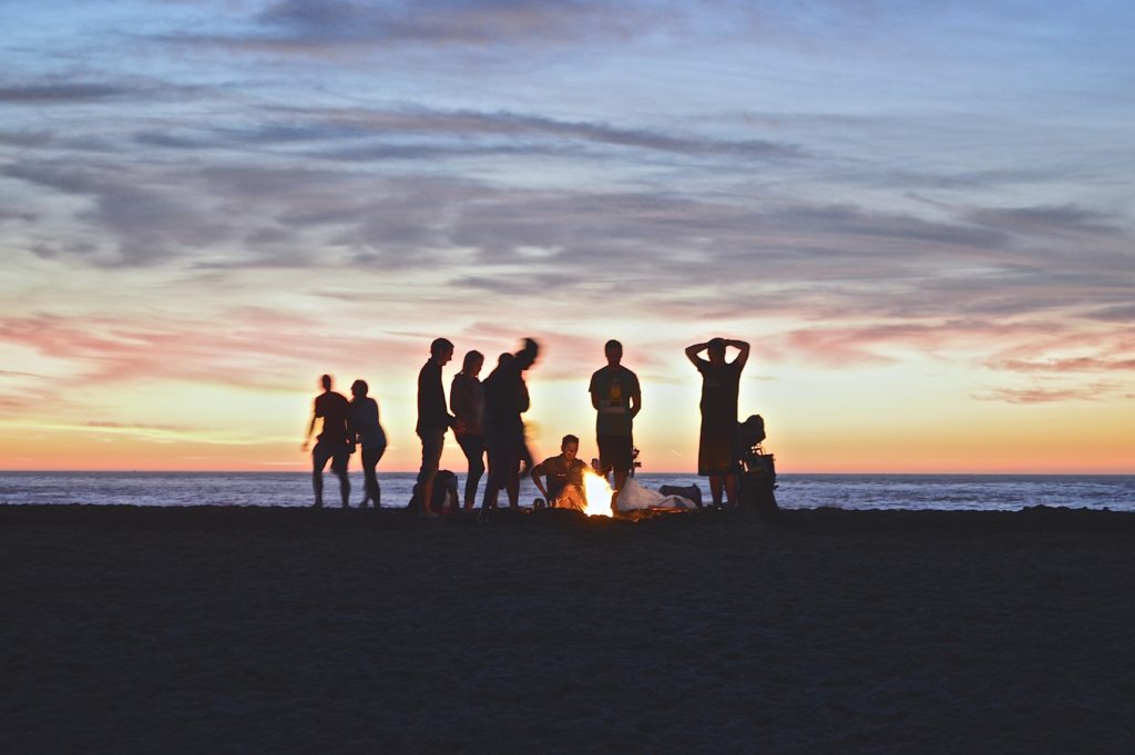 people standing around a bonfire at a beach with the sunset in the background