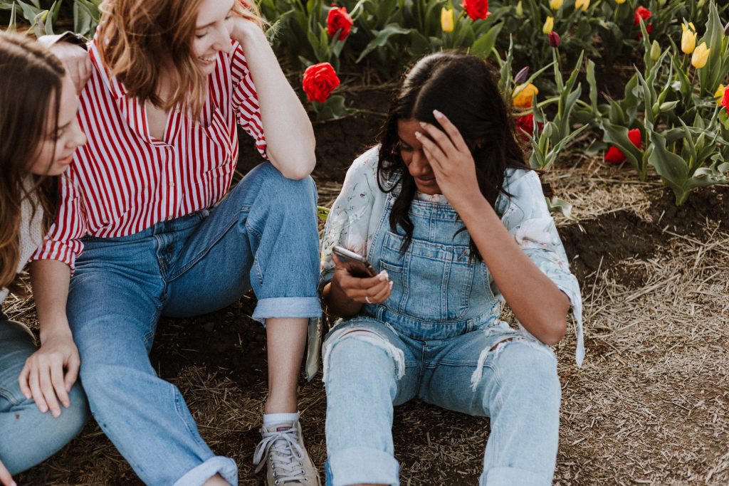 Three girls sitting in a garden laughing together. 