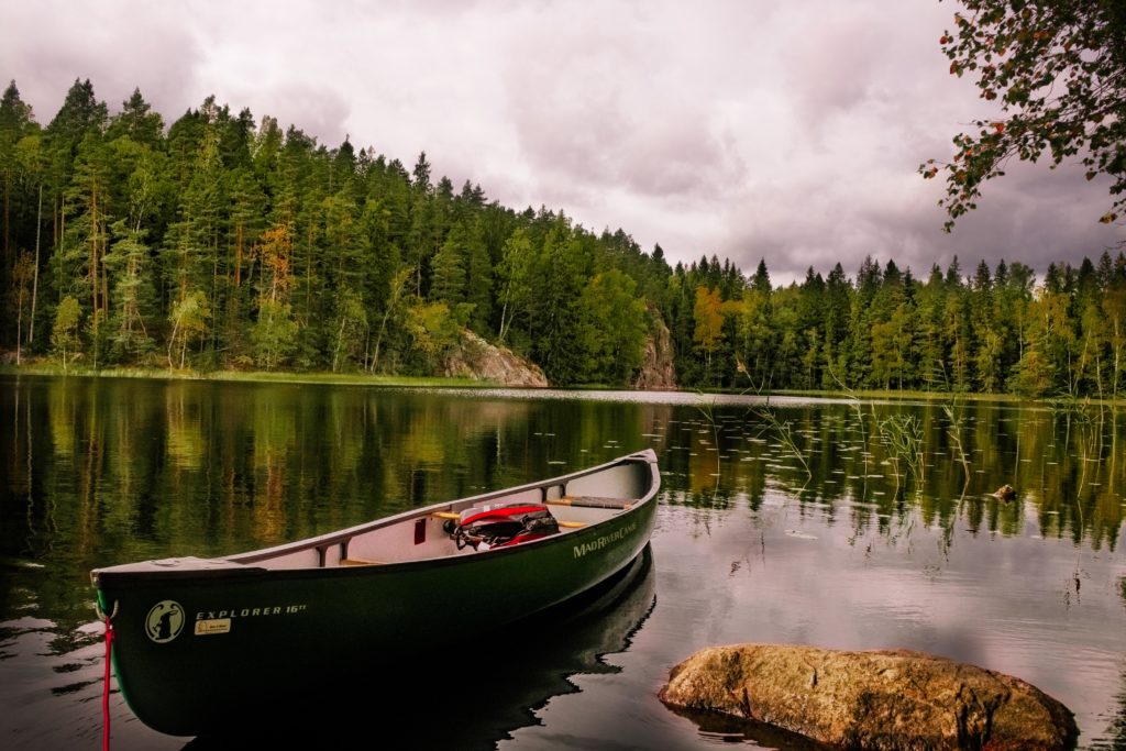 Ein kleines grünes Boot liegt an Land auf einem kleines See und an der Küste ist ein grüner Tannenwald.