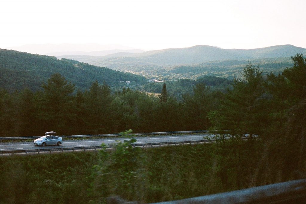 Road trip packing tips: a car on a road with forest surrounding. 