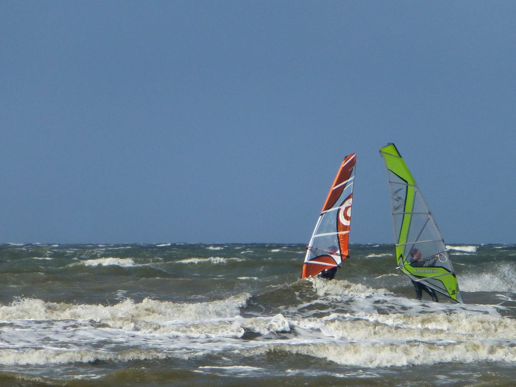 Zwei Windsurfer auf den rauen Wellen vor St. Peter-Ording unter blauem Himmel