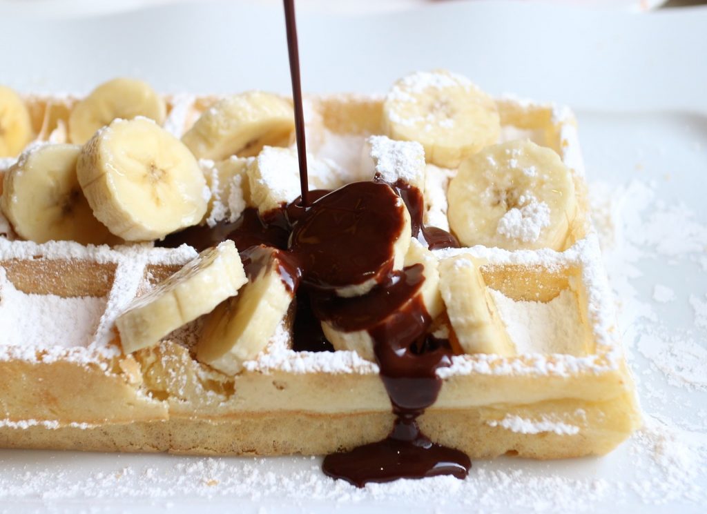 Waffles with bananas and chocolate syrup running over it.
