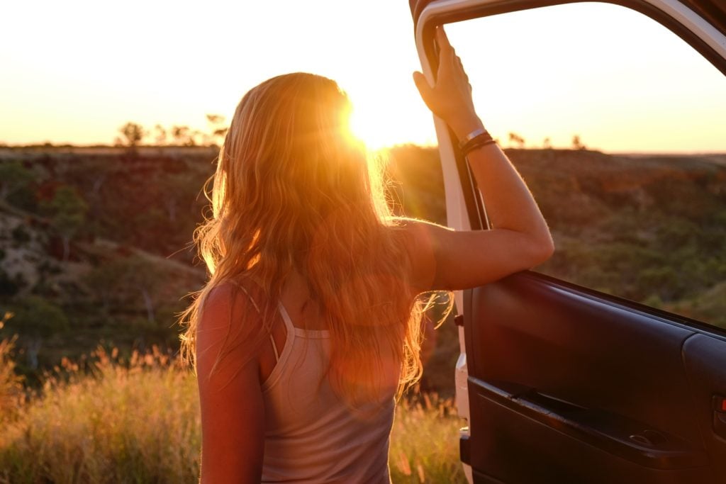 Woman standing on a open car door in sunset tips for a road trip