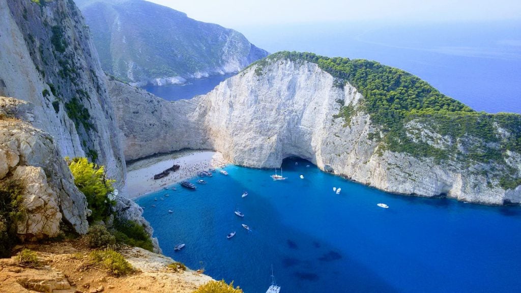 Navagio Beach in Zakynthos with limestone cliffs and blue water as seen from above