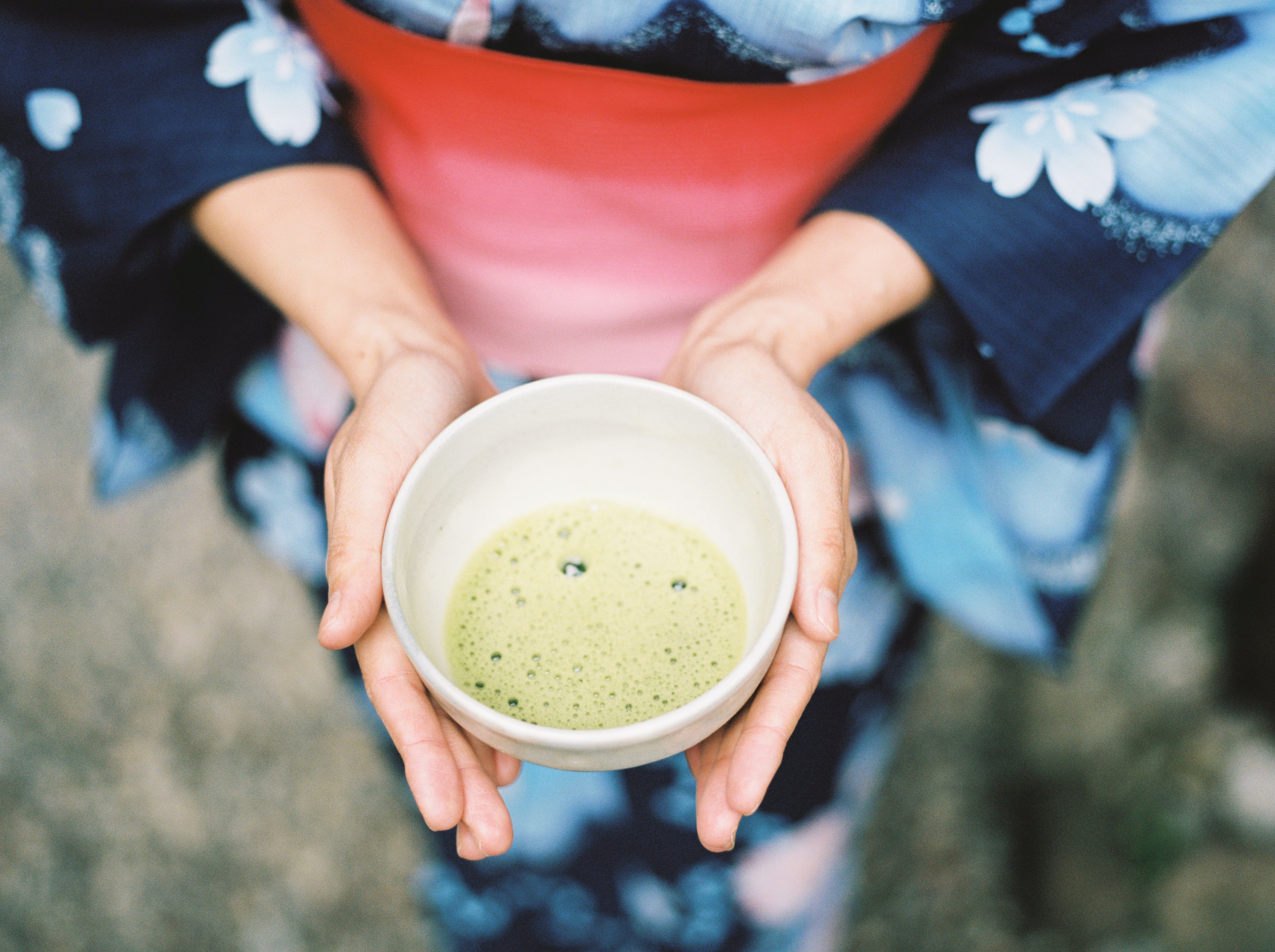 A person in typical Japanese clothing holds a cup of matcha to the camera.