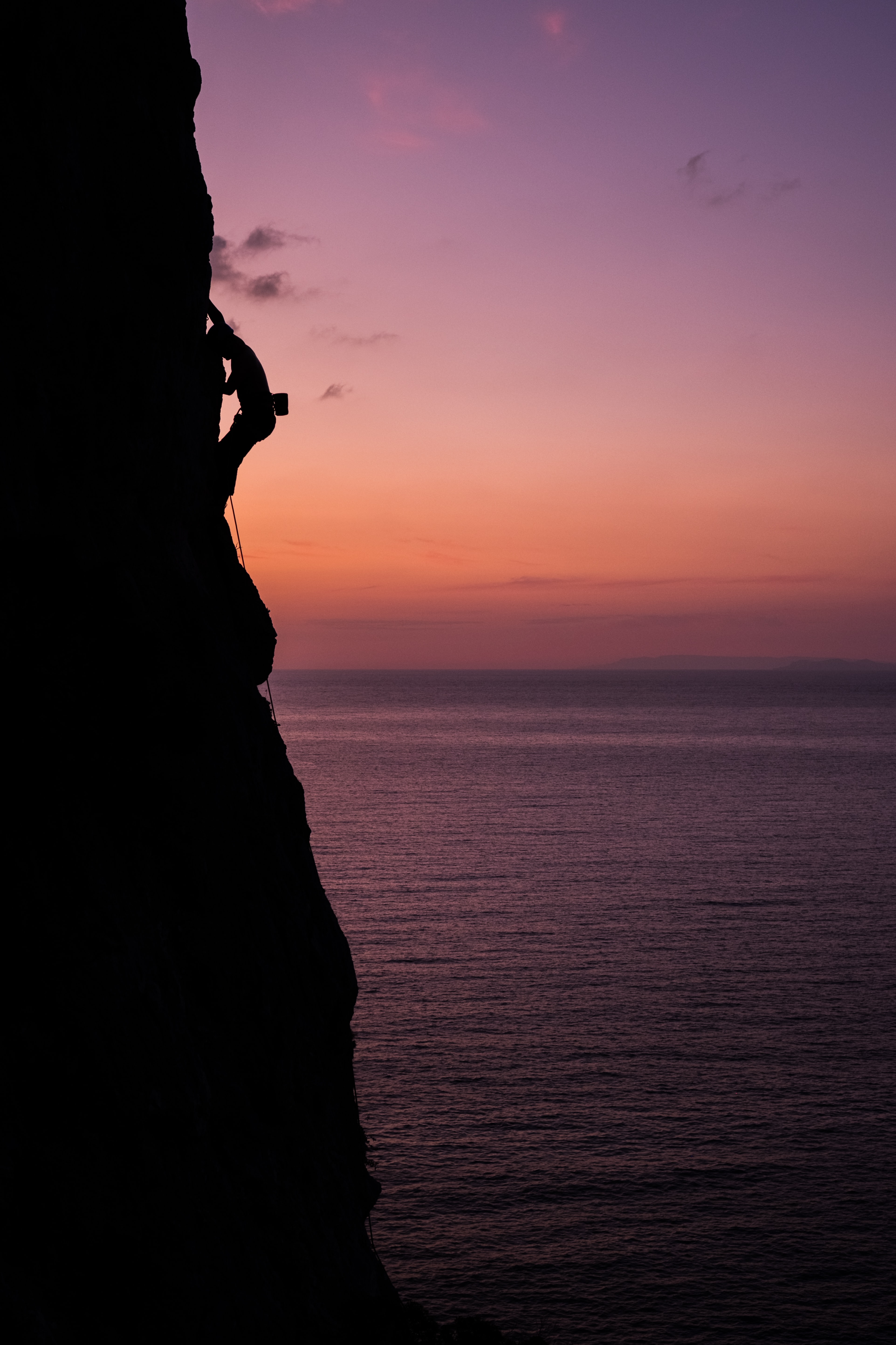 Climbers on a cliff above the Mediterranean Sea in the sunset.