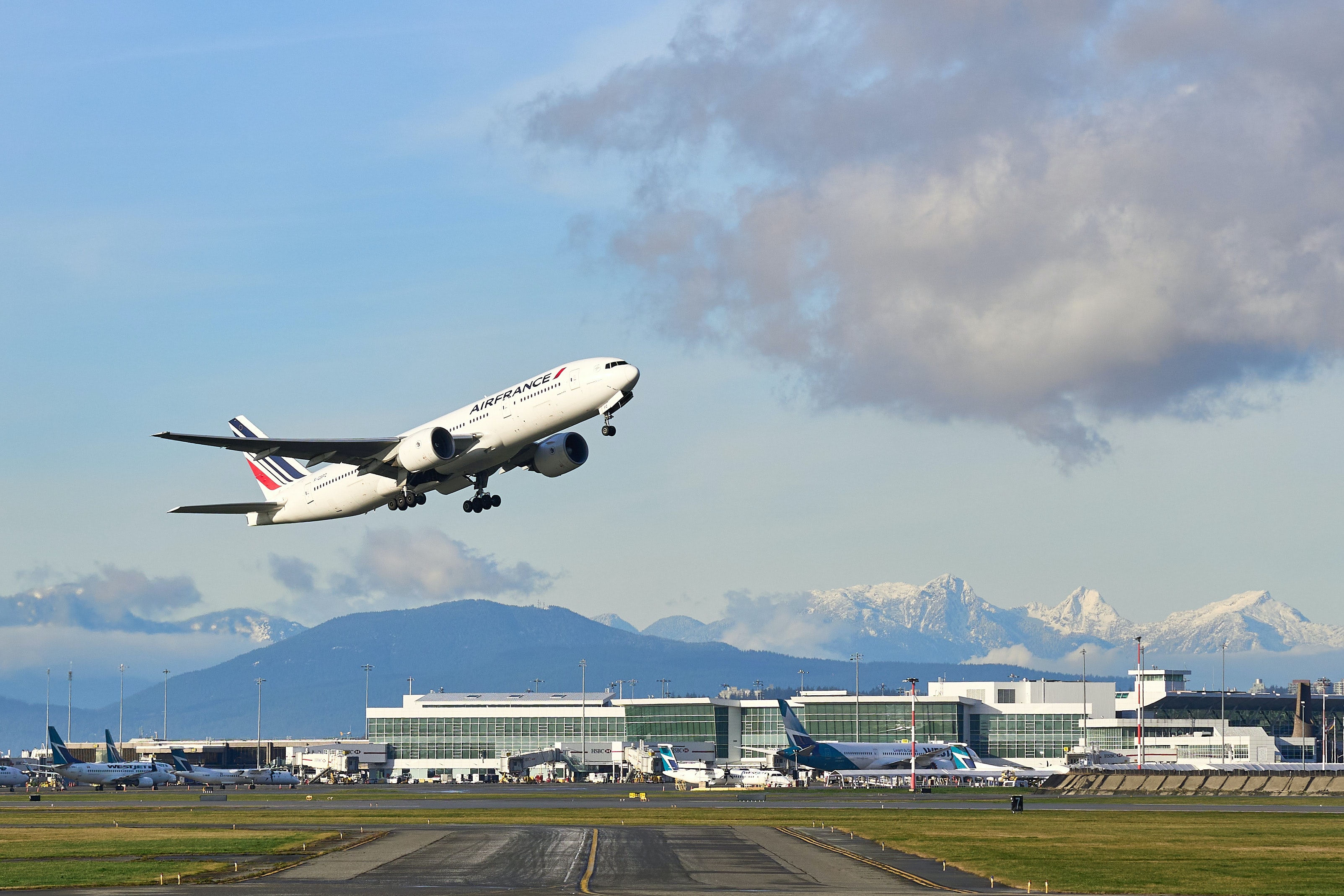 Ein Flugzeug hebt vor der beeindruckenden Kulisse des Flughafens in Vancouver ab, im Hintergrund sieht man Berge.