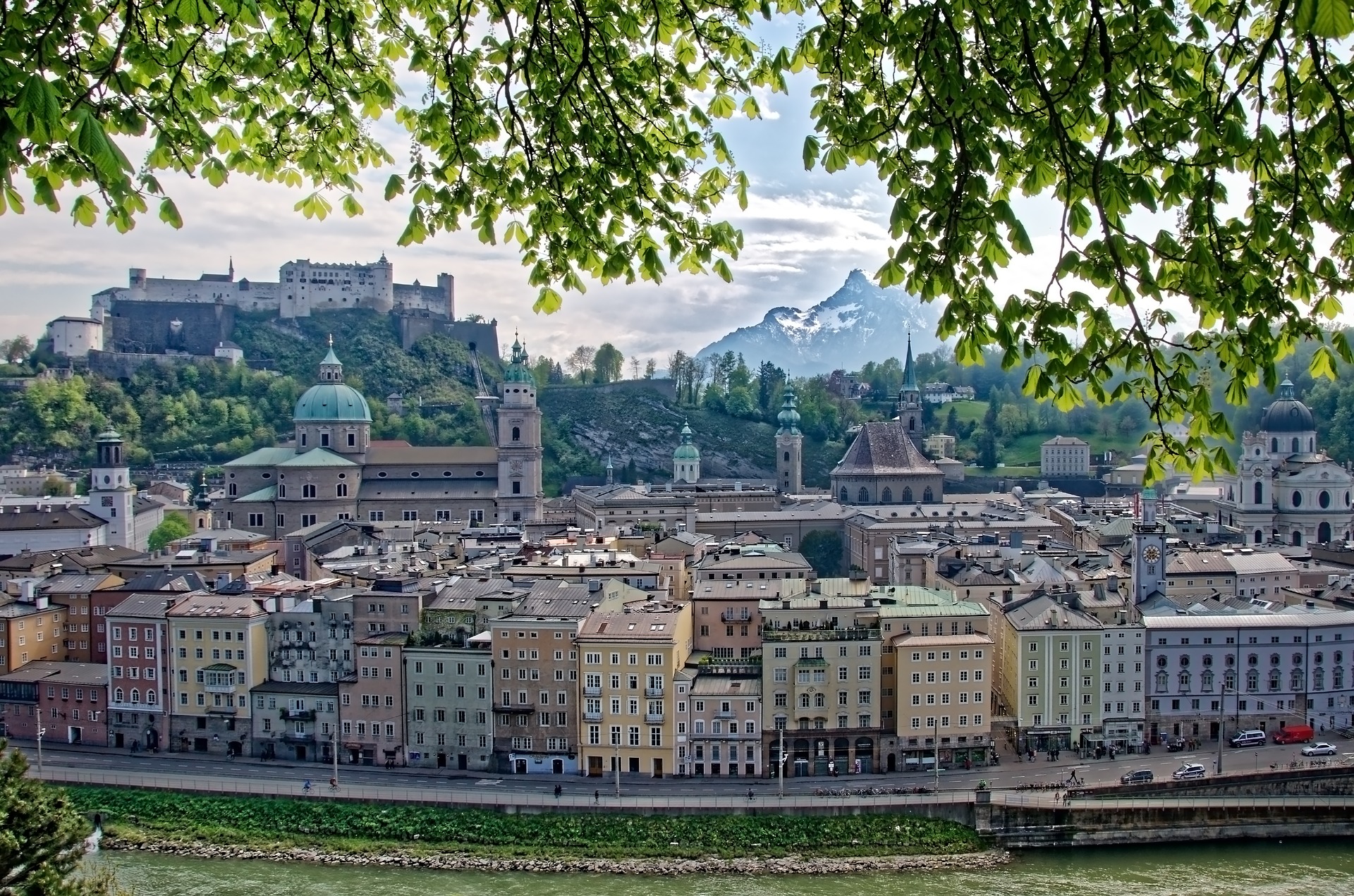 Colorful buildings and a castle with mountains in the background in the city of Salzburg, as pictured from above