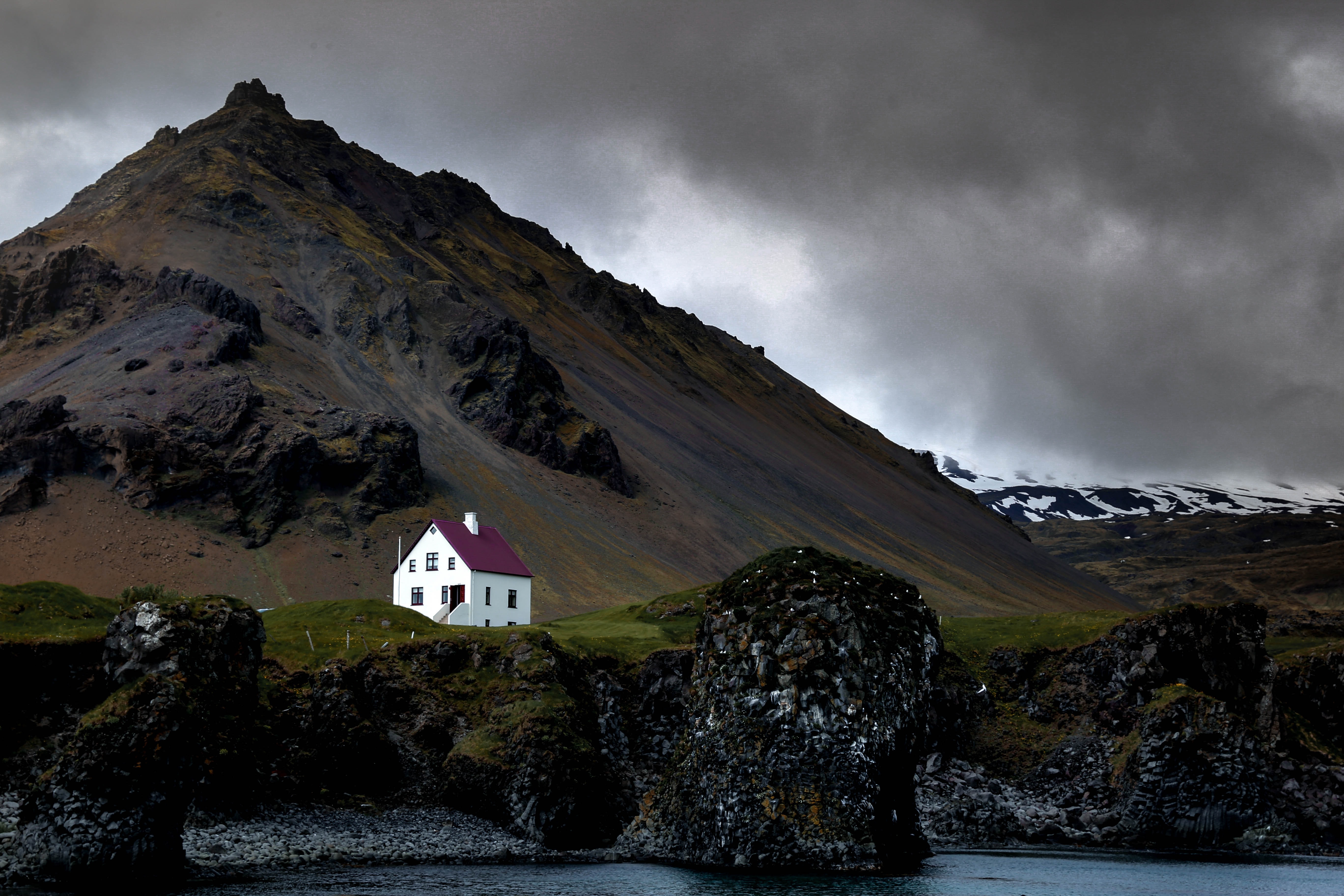 Eine weiße Hütte vor den stimmungsvollen Klippen Islands.