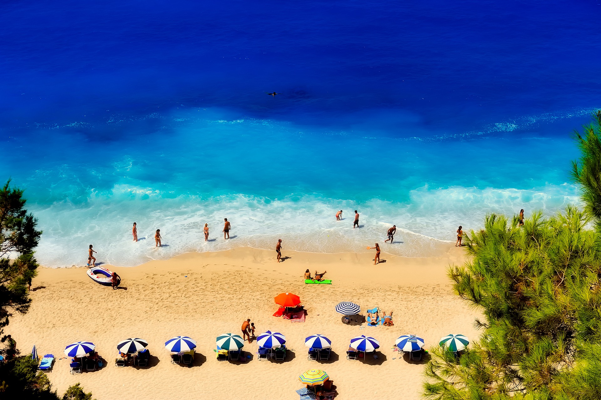Blick auf einen bevölkerten Strand an dem viele Menschen entsapnnen und schwimmen. Man sieht viele bunte Sonnenschirme.
