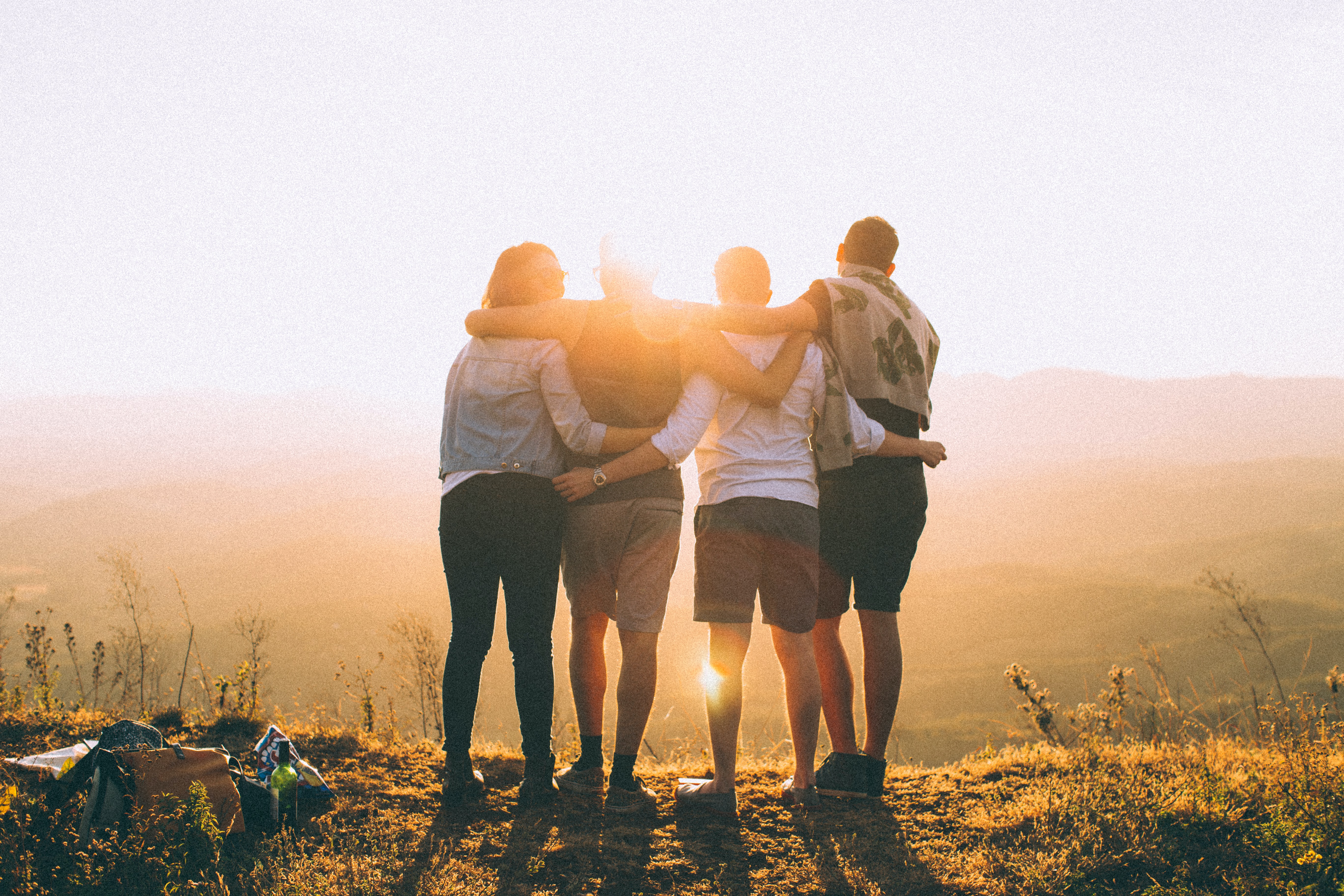 Four friends standing with arms around each other at sunset