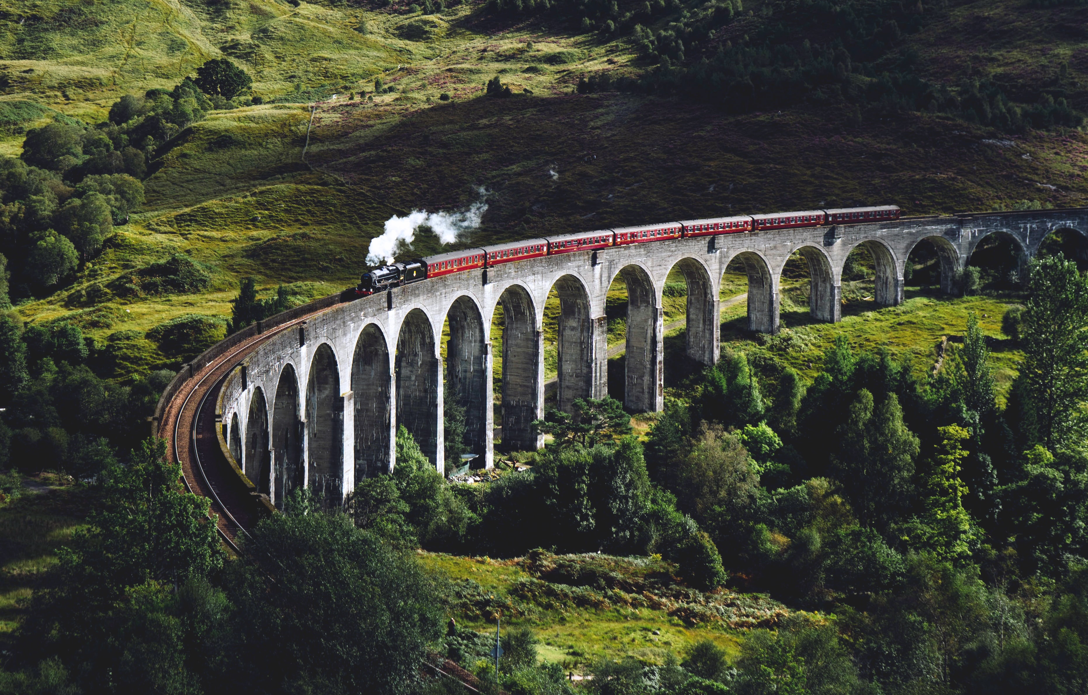 Steam train passing over an arched bridge in hilly landscapes of Scotland