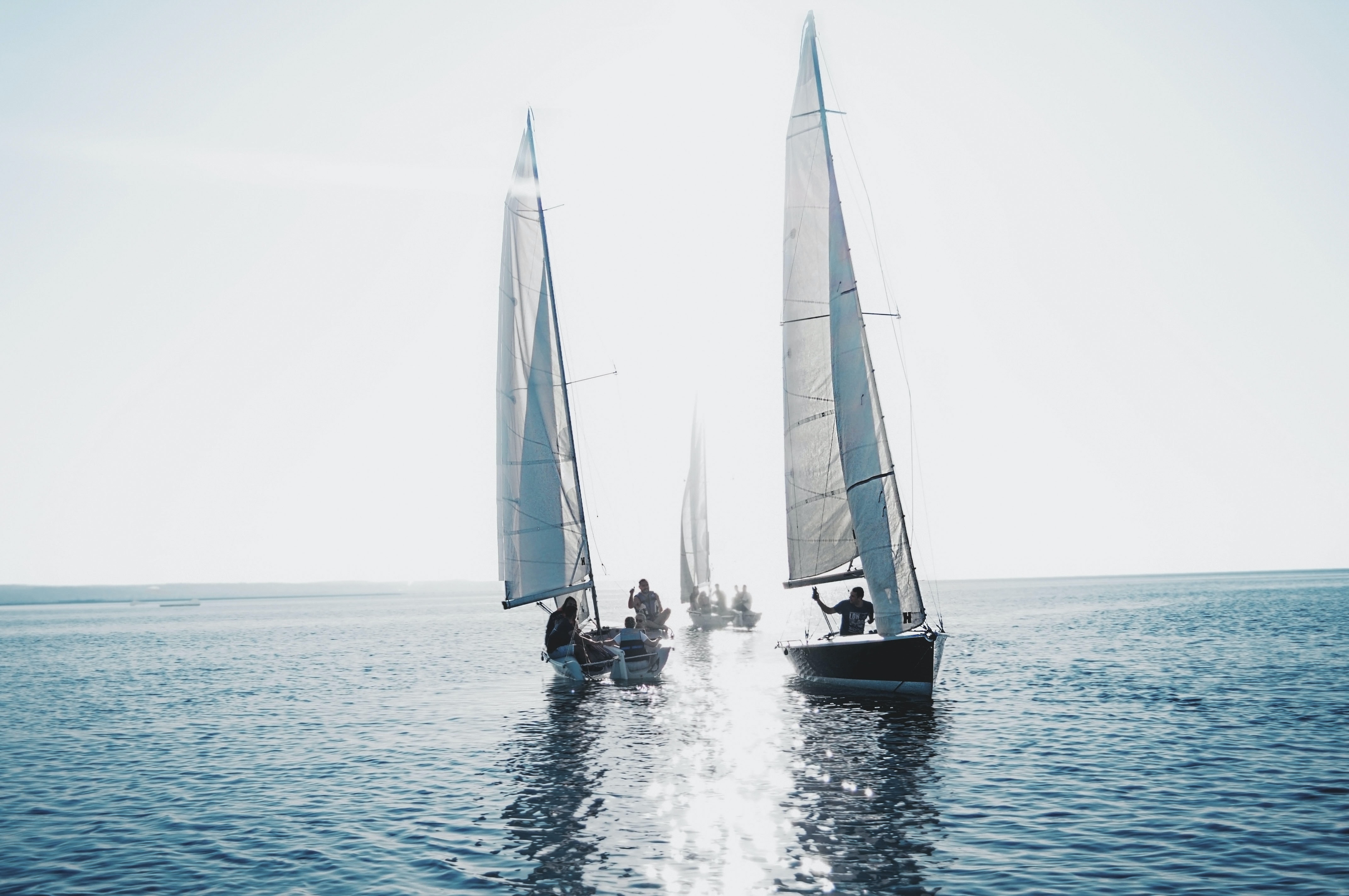 Three sailboats on the water with people