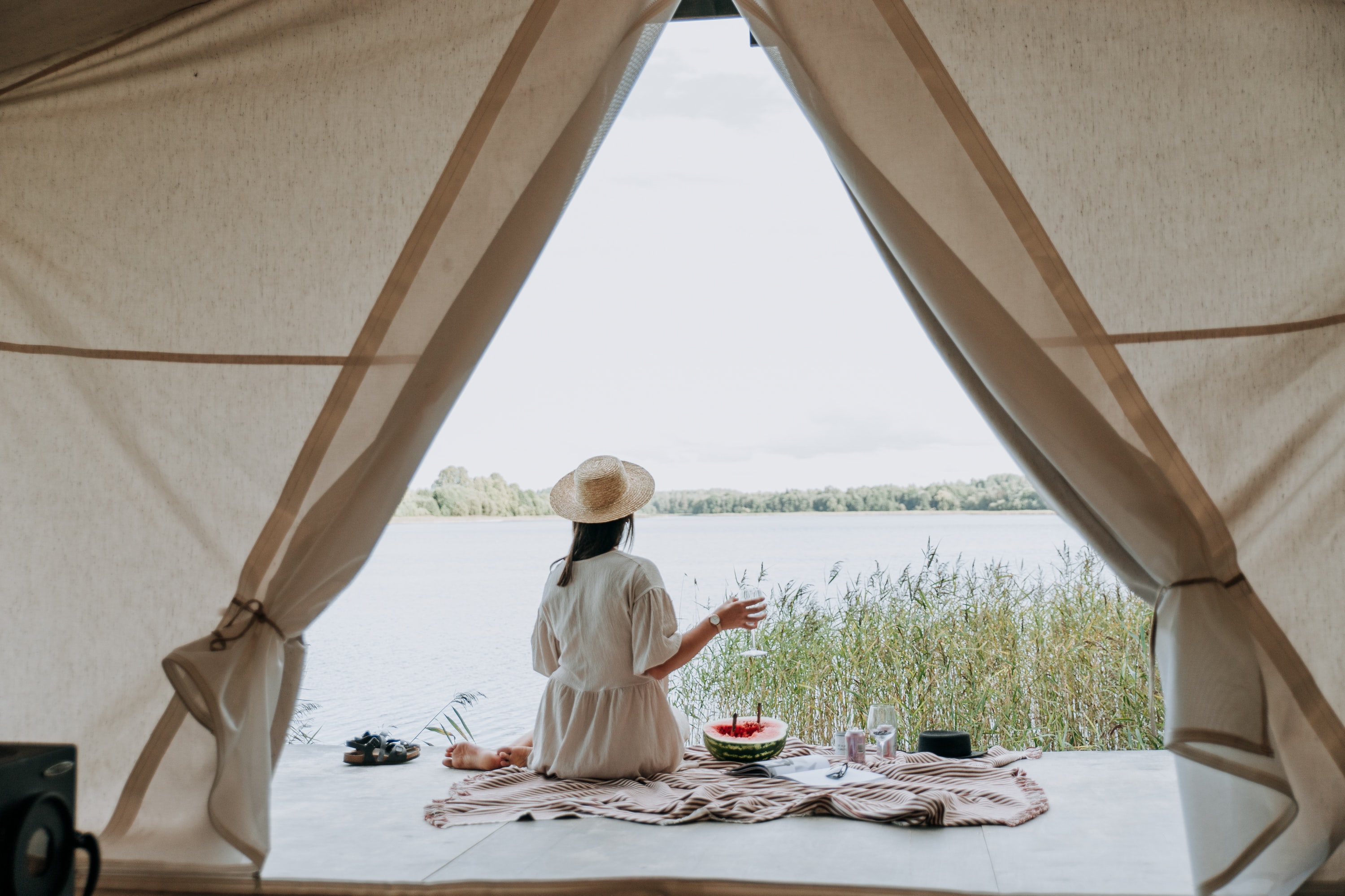 A woman by a lake on a dock pictured from inside a tent
