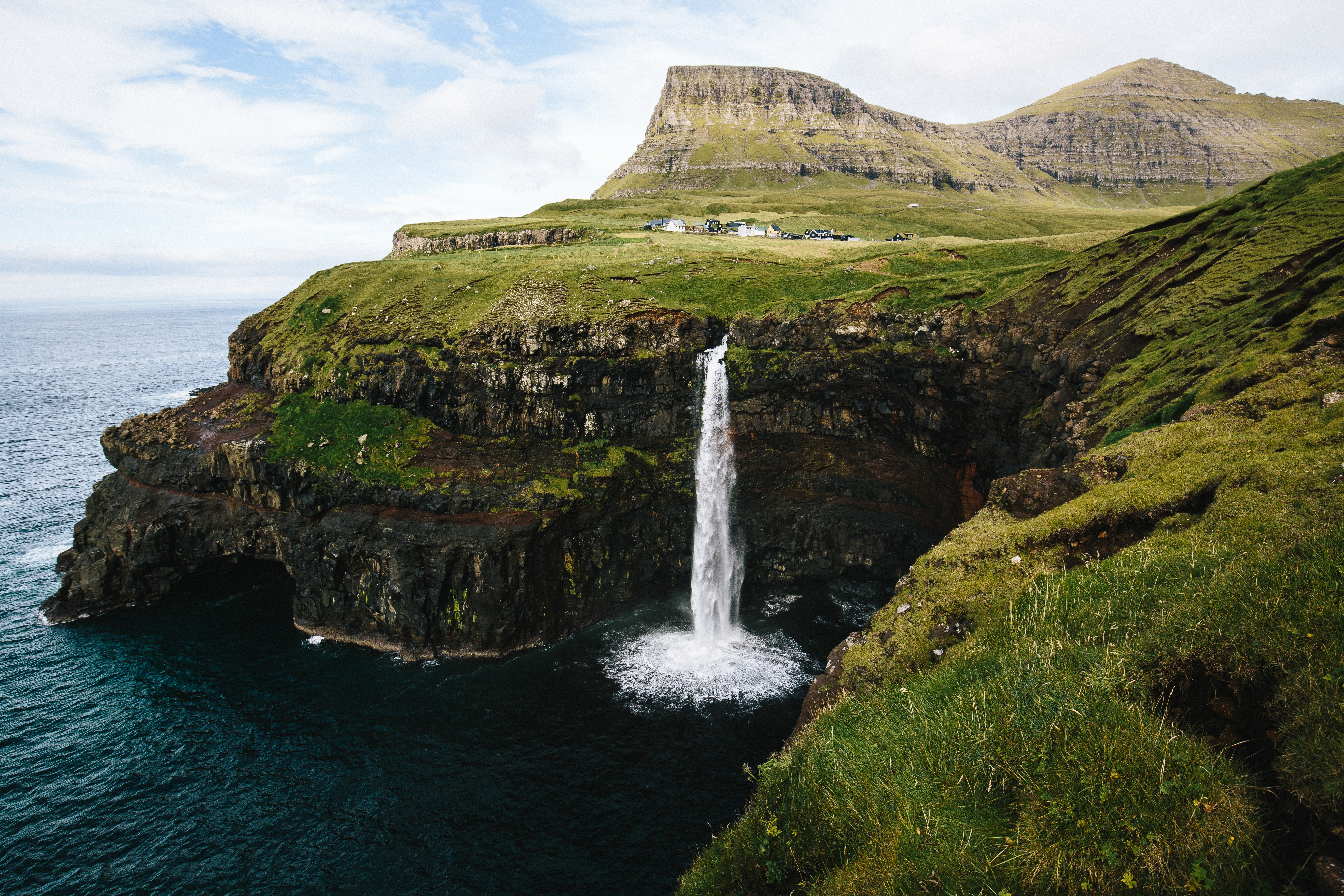 Eine zerklüftete Landschaft und ein Wasserfall der direkt ins Meer fließt auf den Faröer Inseln.
