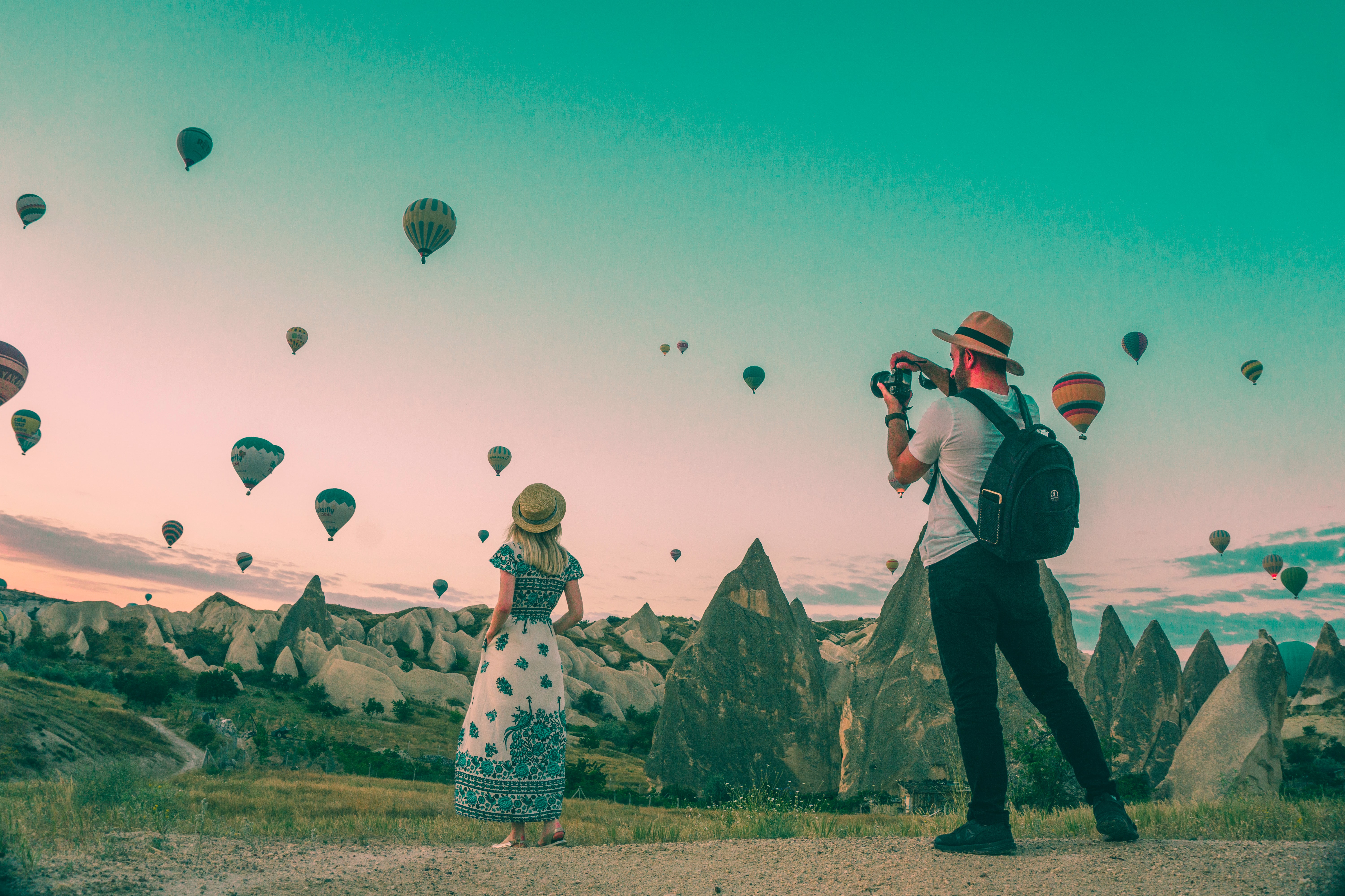 Two people taking pictures surrounded by rock structures and hot air balloons