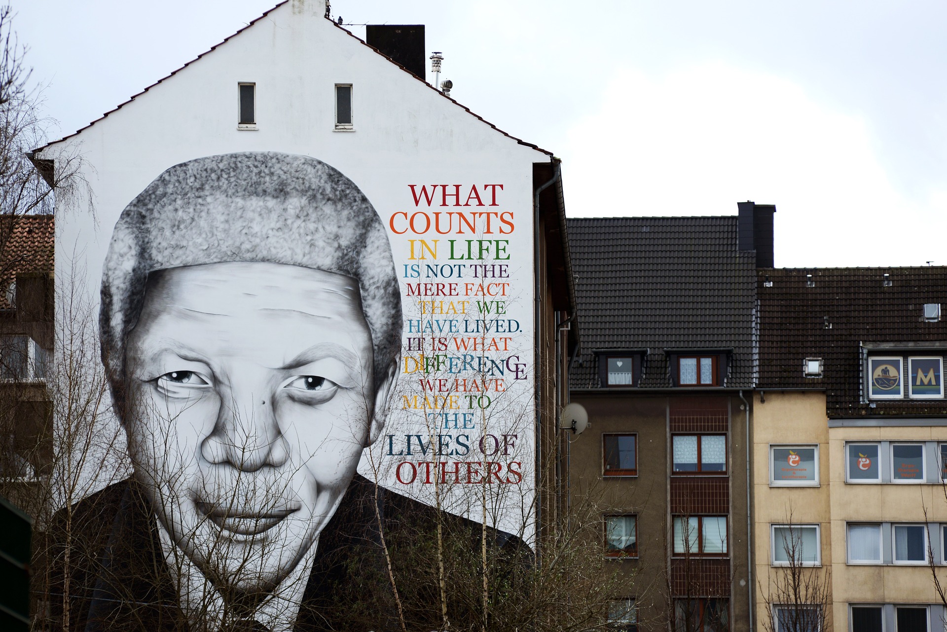 Ein Straßenkunst Portrait von Mandela auf einer Hauswand mit einem berühmten Zitat.
