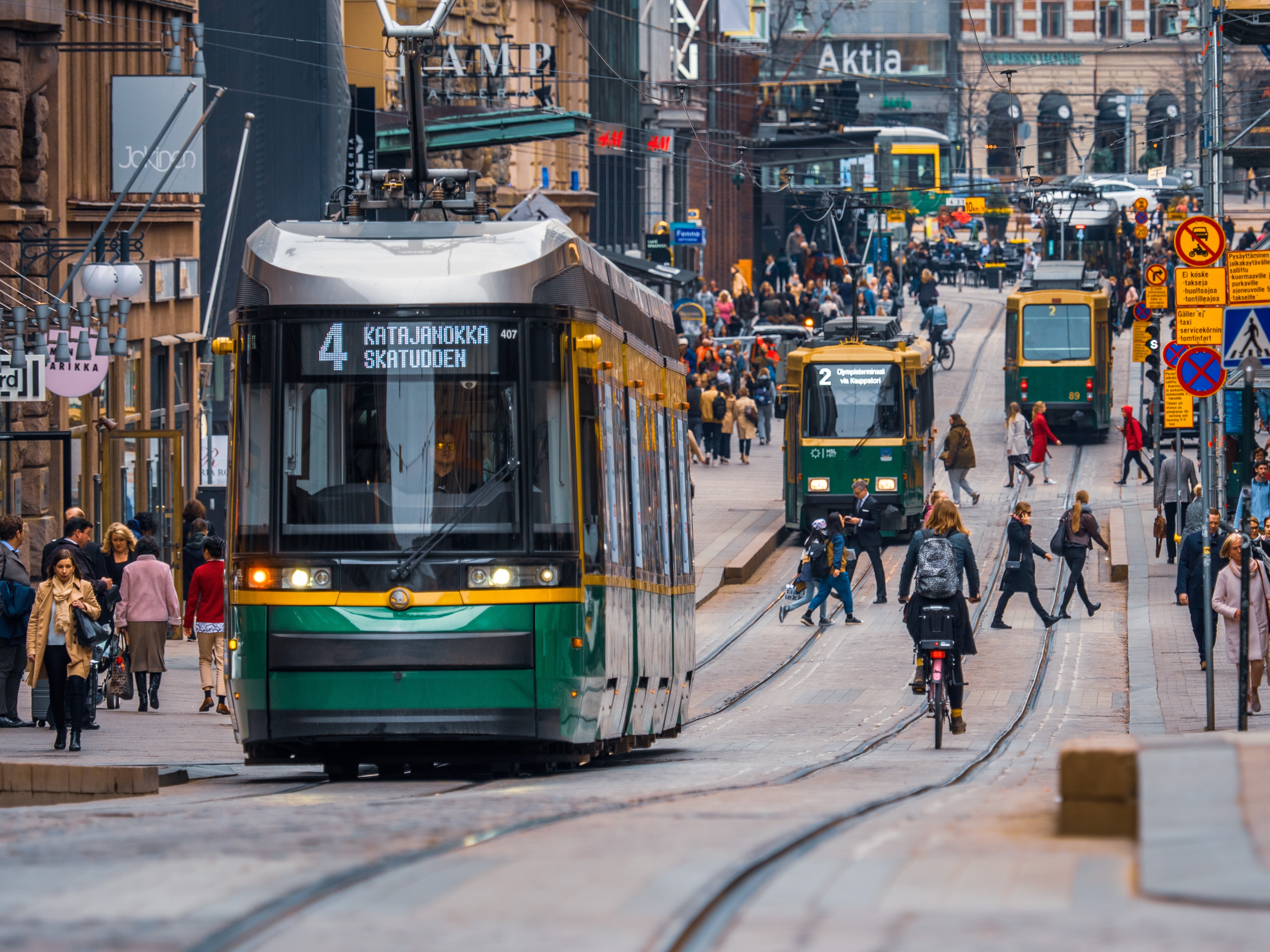 Trams and people walking and biking on a street in Helsinki